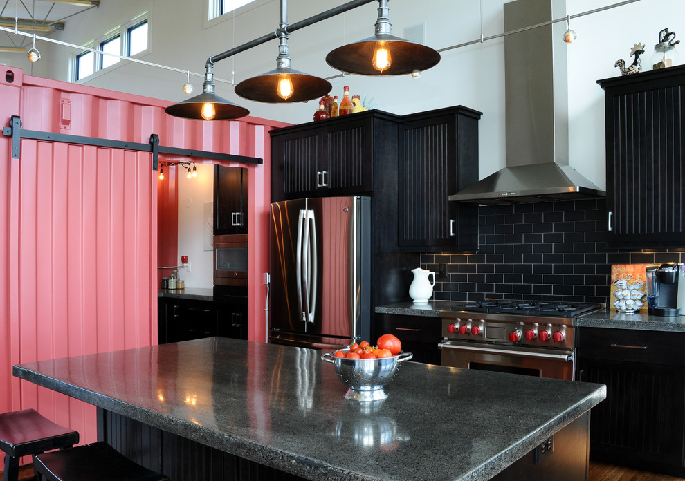 Photo of a mid-sized industrial single-wall open plan kitchen in Other with black cabinets, black splashback, stainless steel appliances, medium hardwood floors, with island, recessed-panel cabinets, concrete benchtops and ceramic splashback.