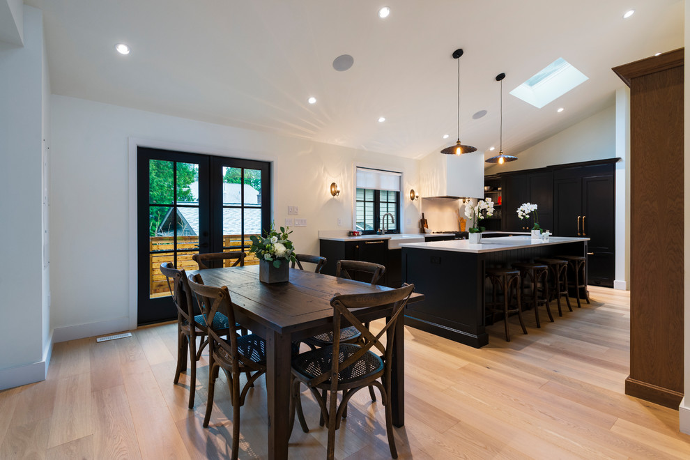 Open concept kitchen - mid-sized rustic l-shaped light wood floor and beige floor open concept kitchen idea in Vancouver with a farmhouse sink, shaker cabinets, black cabinets, quartz countertops, paneled appliances, an island and white countertops