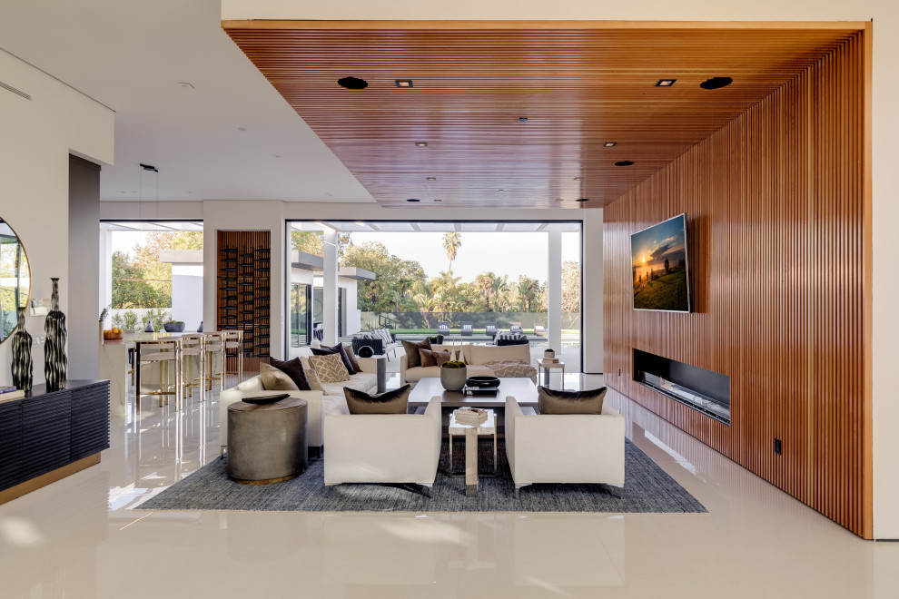 Inspiration for an expansive contemporary open concept family room in Los Angeles with brown walls, porcelain floors, a standard fireplace, a wood fireplace surround, a wall-mounted tv and white floor.