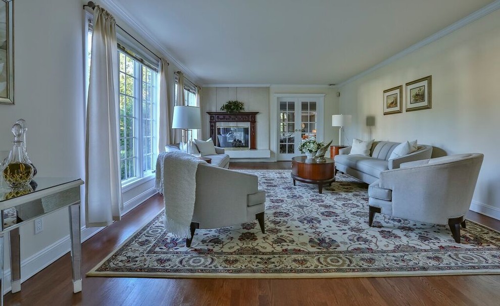 This is an example of a large traditional enclosed living room in New York with white walls, medium hardwood floors, a standard fireplace, a wood fireplace surround, no tv and brown floor.