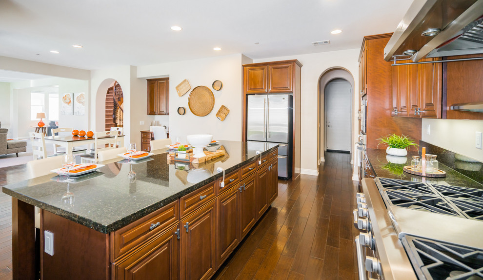 Inspiration for a large transitional u-shaped dark wood floor and brown floor kitchen remodel in Los Angeles with an undermount sink, raised-panel cabinets, medium tone wood cabinets, granite countertops, stainless steel appliances and an island