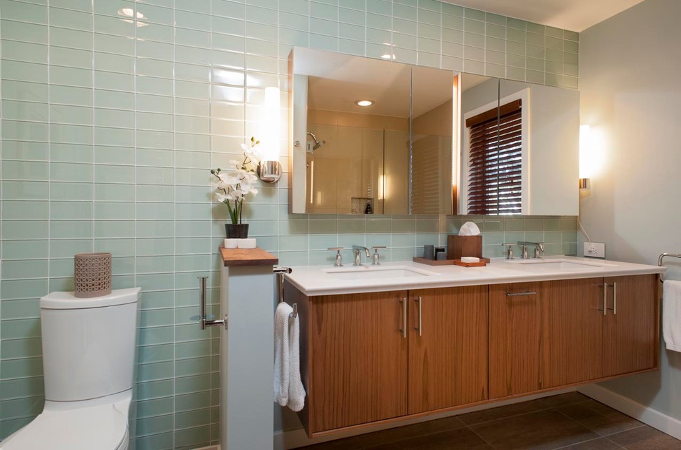 Photo of a mid-sized modern master bathroom in Bridgeport with an integrated sink, flat-panel cabinets, medium wood cabinets, solid surface benchtops, a one-piece toilet, green tile, glass tile, grey walls and ceramic floors.