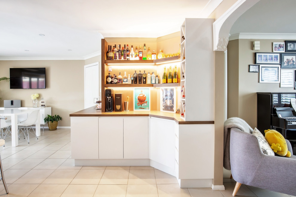 Photo of a small contemporary l-shaped home bar in Sydney with flat-panel cabinets, white cabinets, wood benchtops, beige splashback, glass sheet splashback, porcelain floors and beige floor.