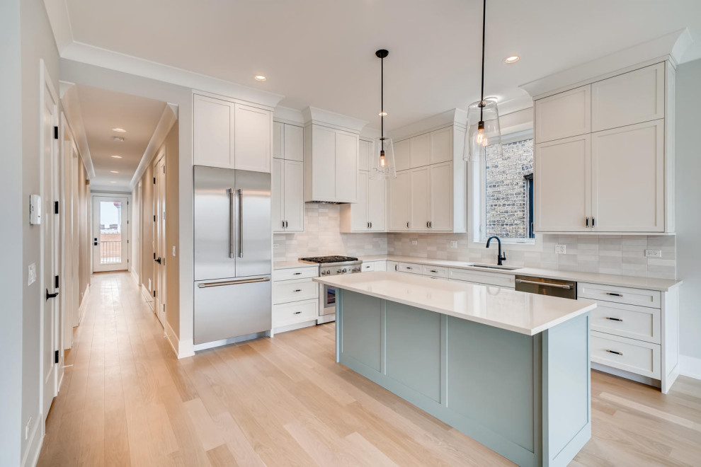 Photo of a mid-sized modern l-shaped eat-in kitchen in Denver with a drop-in sink, flat-panel cabinets, white cabinets, quartzite benchtops, white splashback, marble splashback, stainless steel appliances, light hardwood floors, with island and white benchtop.
