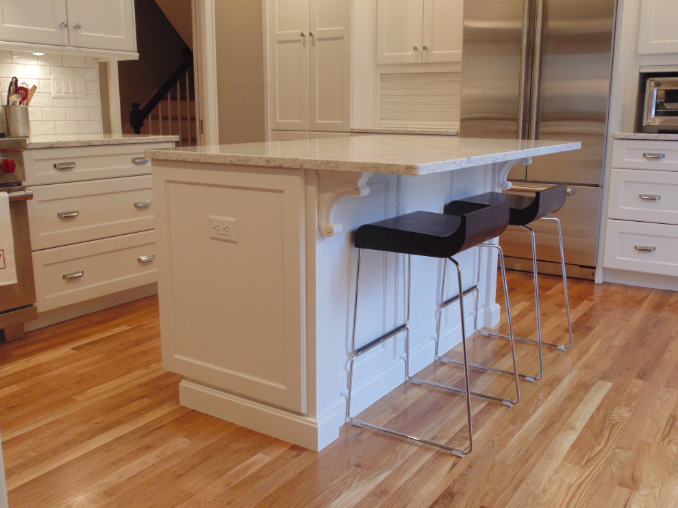 Example of a large transitional u-shaped medium tone wood floor and brown floor eat-in kitchen design with an undermount sink, recessed-panel cabinets, white cabinets, quartz countertops, white backsplash, subway tile backsplash, stainless steel appliances, an island and white countertops