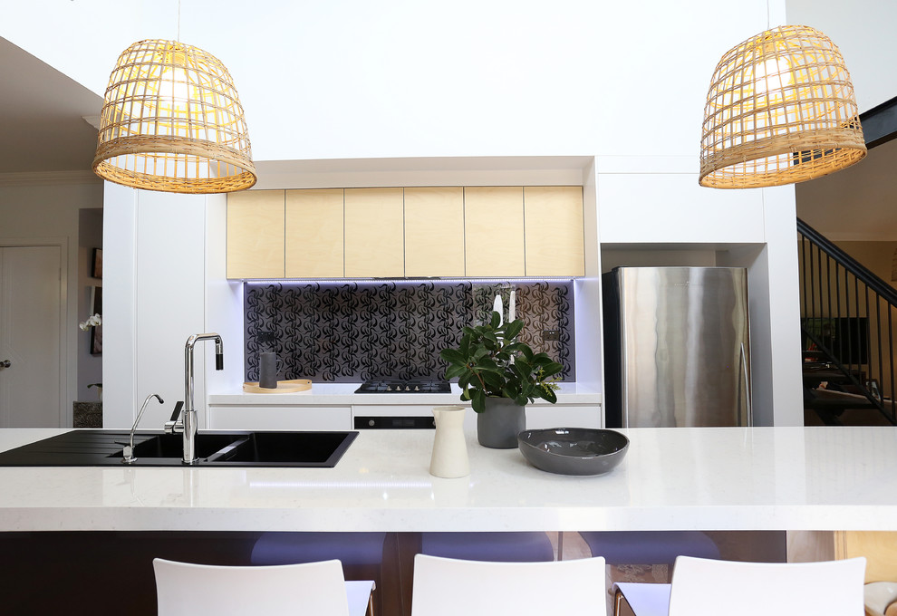Photo of a modern galley kitchen in Brisbane with a double-bowl sink, quartz benchtops, grey splashback, glass sheet splashback, black appliances, medium hardwood floors and with island.