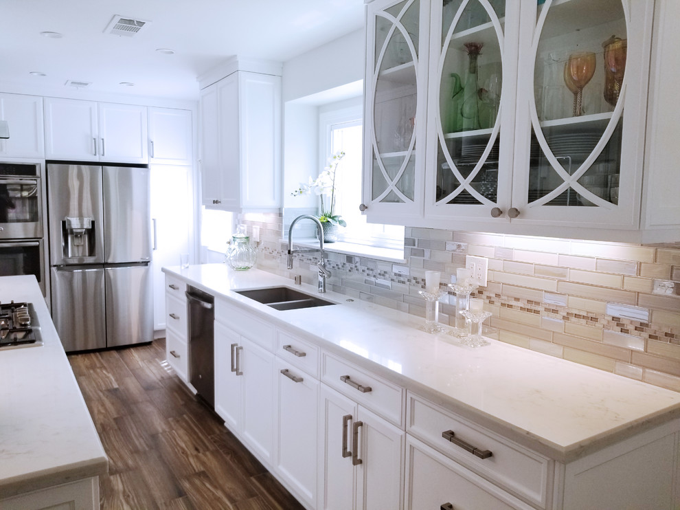 Inspiration for a small traditional galley separate kitchen in Los Angeles with an undermount sink, glass-front cabinets, white cabinets, quartz benchtops, grey splashback, glass tile splashback, stainless steel appliances, porcelain floors, no island and brown floor.