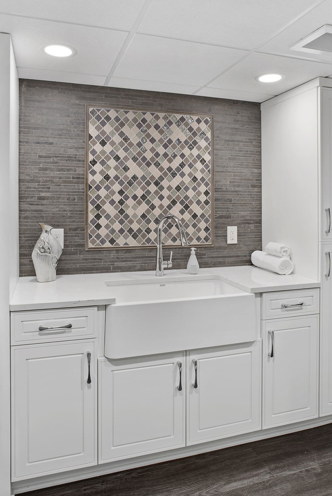 Inspiration for a large transitional single-wall vinyl floor and gray floor dedicated laundry room remodel in Columbus with a farmhouse sink, raised-panel cabinets, white cabinets, quartz countertops, multicolored walls and white countertops