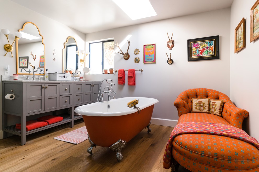 This is an example of a large bathroom in Los Angeles with grey cabinets, a claw-foot tub, medium hardwood floors, brown floor, shaker cabinets, grey walls, an undermount sink, marble benchtops and white benchtops.