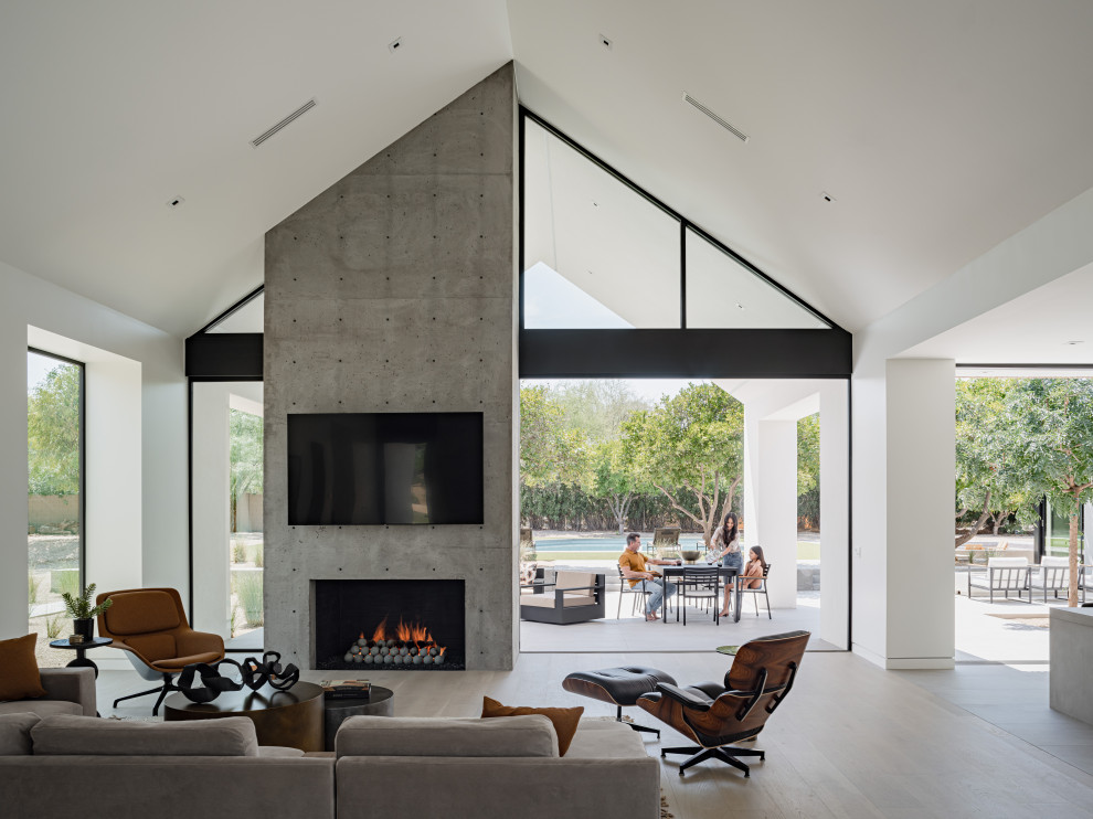 Example of a minimalist open concept light wood floor and vaulted ceiling living room design in Phoenix with white walls, a standard fireplace, a concrete fireplace and a wall-mounted tv