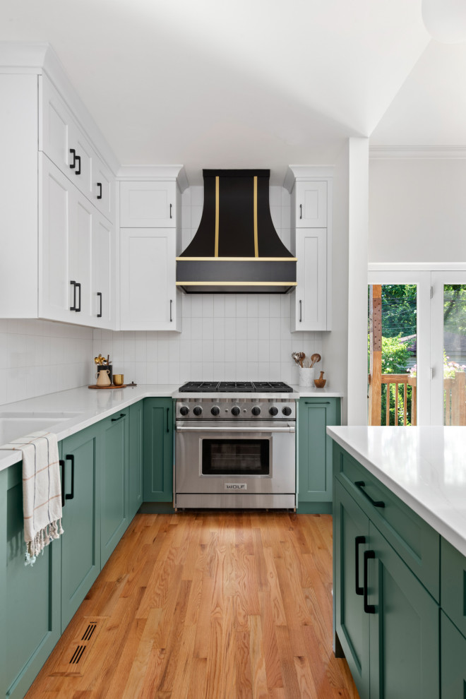シカゴにある高級な中くらいなトラディショナルスタイルのおしゃれなキッチン (ドロップインシンク、シェーカースタイル扉のキャビネット、緑のキャビネット、クオーツストーンカウンター、白いキッチンパネル、セラミックタイルのキッチンパネル、黒い調理設備、無垢フローリング、茶色い床、白いキッチンカウンター) の写真