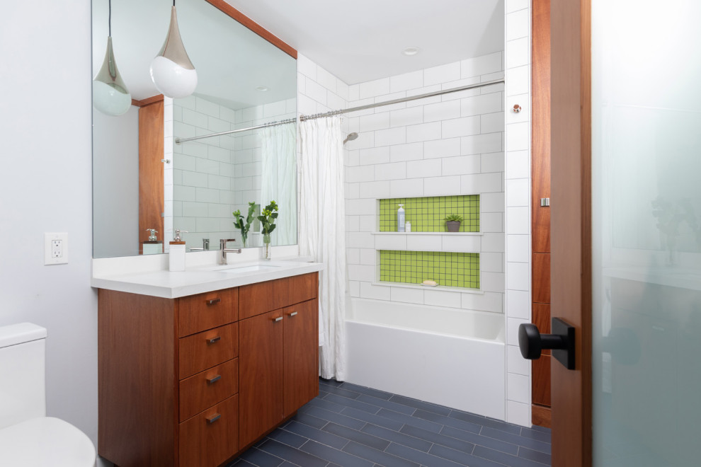 Medium sized modern family bathroom in Los Angeles with flat-panel cabinets, medium wood cabinets, an alcove bath, a shower/bath combination, a one-piece toilet, white tiles, ceramic tiles, porcelain flooring, a submerged sink, engineered stone worktops, blue floors, white worktops, a wall niche, a single sink and a built in vanity unit.
