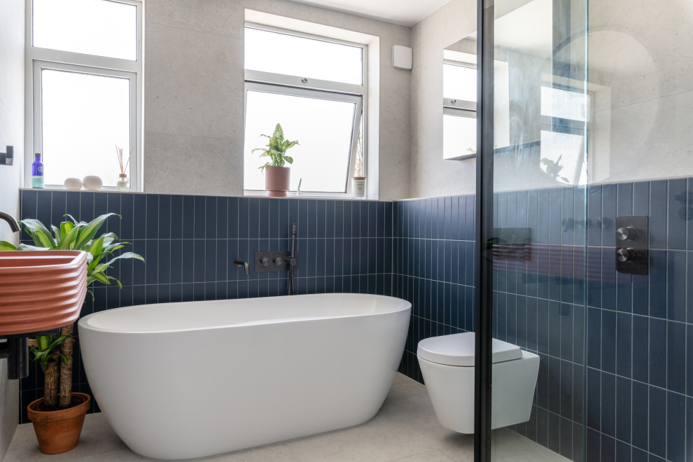 This is an example of a medium sized contemporary family bathroom in London with a freestanding bath, a walk-in shower, a one-piece toilet, grey tiles, porcelain tiles, grey walls, porcelain flooring, a wall-mounted sink, concrete worktops, grey floors, a hinged door, orange worktops and a single sink.