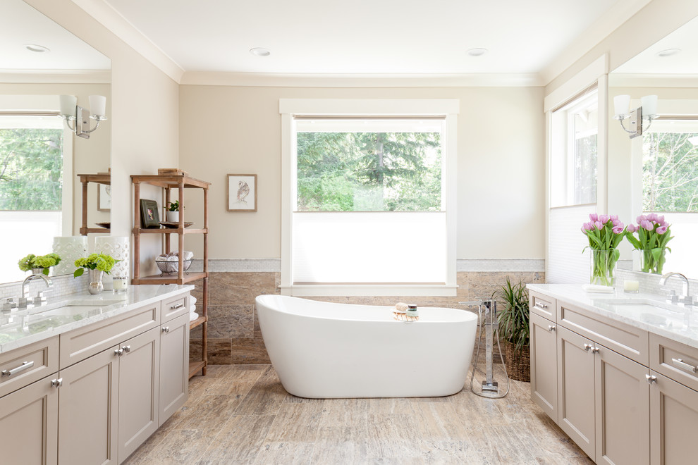 Photo of a large transitional master bathroom in Seattle with shaker cabinets, grey cabinets, a freestanding tub, an alcove shower, a two-piece toilet, multi-coloured tile, brown tile, travertine, grey walls, travertine floors, an undermount sink, marble benchtops, a hinged shower door and brown floor.