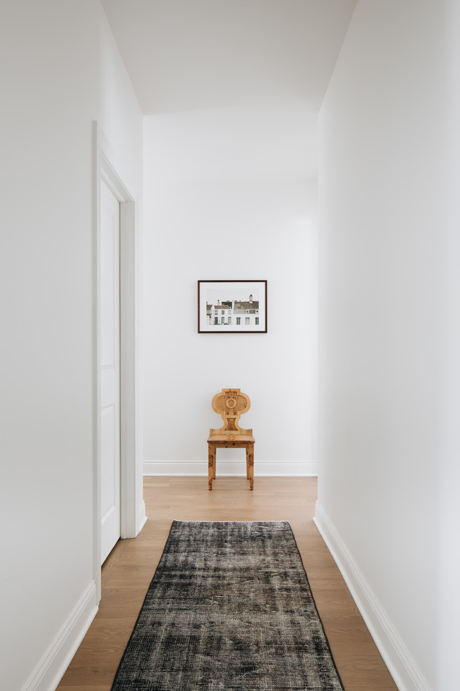Inspiration for a mid-sized transitional hallway in Chicago with white walls, light hardwood floors and brown floor.