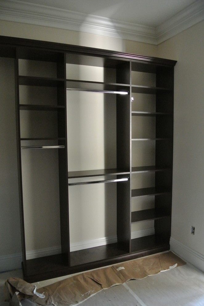 This is an example of a large classic gender neutral walk-in wardrobe in Miami with raised-panel cabinets, dark wood cabinets and travertine flooring.