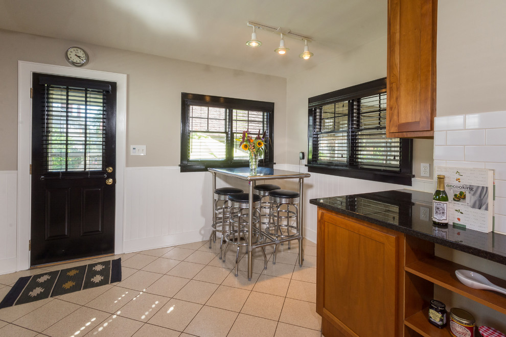 Photo of a mid-sized eclectic eat-in kitchen in Columbus with a double-bowl sink, flat-panel cabinets, medium wood cabinets, granite benchtops, white splashback, subway tile splashback, stainless steel appliances, ceramic floors and no island.