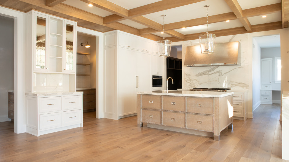 Modern inredning av ett mellanstort vit vitt kök, med luckor med profilerade fronter, vita skåp, marmorbänkskiva, vitt stänkskydd, stänkskydd i marmor, ljust trägolv, en köksö och brunt golv