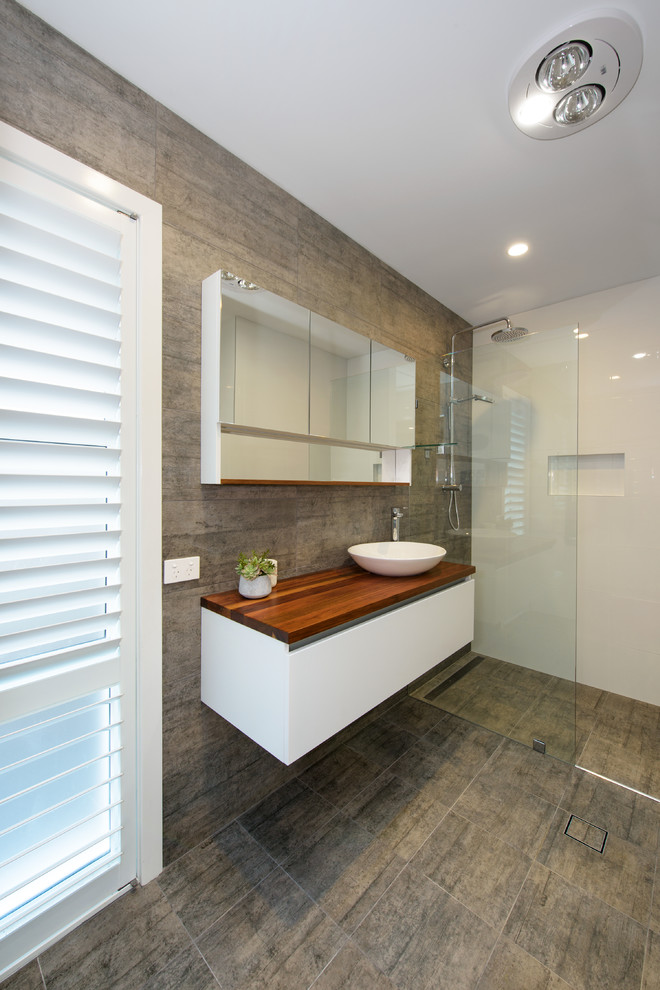 This is an example of a small contemporary master bathroom in Central Coast with white cabinets, a double shower, a one-piece toilet, gray tile, ceramic tile, white walls, ceramic floors, a vessel sink, wood benchtops, grey floor and an open shower.