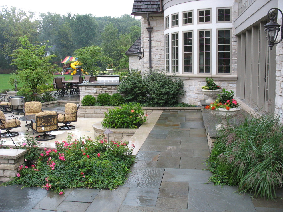 This is an example of a traditional backyard patio in Chicago with natural stone pavers and no cover.