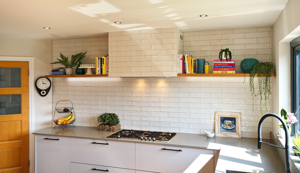 This is an example of a mid-sized industrial l-shaped eat-in kitchen in Other with a drop-in sink, flat-panel cabinets, grey cabinets, quartzite benchtops, white splashback, ceramic splashback, stainless steel appliances, laminate floors, with island, brown floor and grey benchtop.