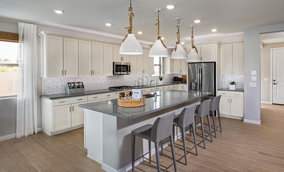 Design ideas for a mid-sized contemporary l-shaped open plan kitchen in Phoenix with an undermount sink, shaker cabinets, white cabinets, quartz benchtops, white splashback, porcelain splashback, stainless steel appliances, medium hardwood floors, with island, beige floor and grey benchtop.