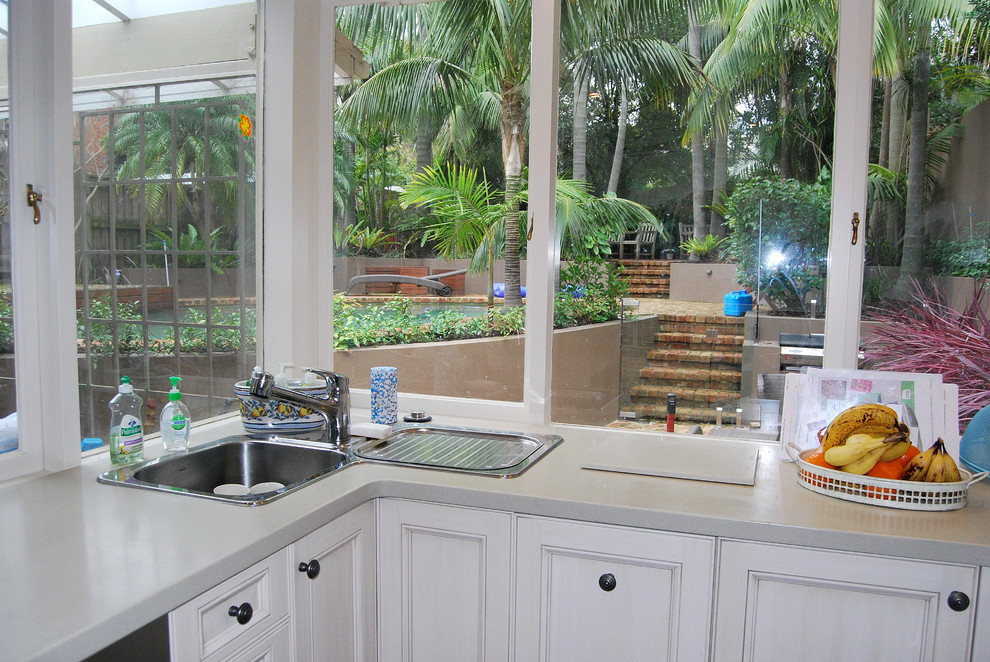 Design ideas for a mid-sized traditional u-shaped kitchen pantry in Sydney with a drop-in sink, shaker cabinets, beige cabinets, solid surface benchtops, beige splashback, porcelain splashback, stainless steel appliances, slate floors and a peninsula.