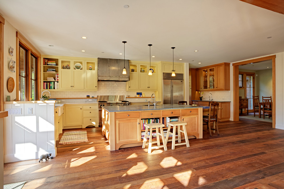 Mid-sized traditional l-shaped open plan kitchen in Austin with a farmhouse sink, shaker cabinets, yellow cabinets, soapstone benchtops, white splashback, subway tile splashback, stainless steel appliances, dark hardwood floors and with island.