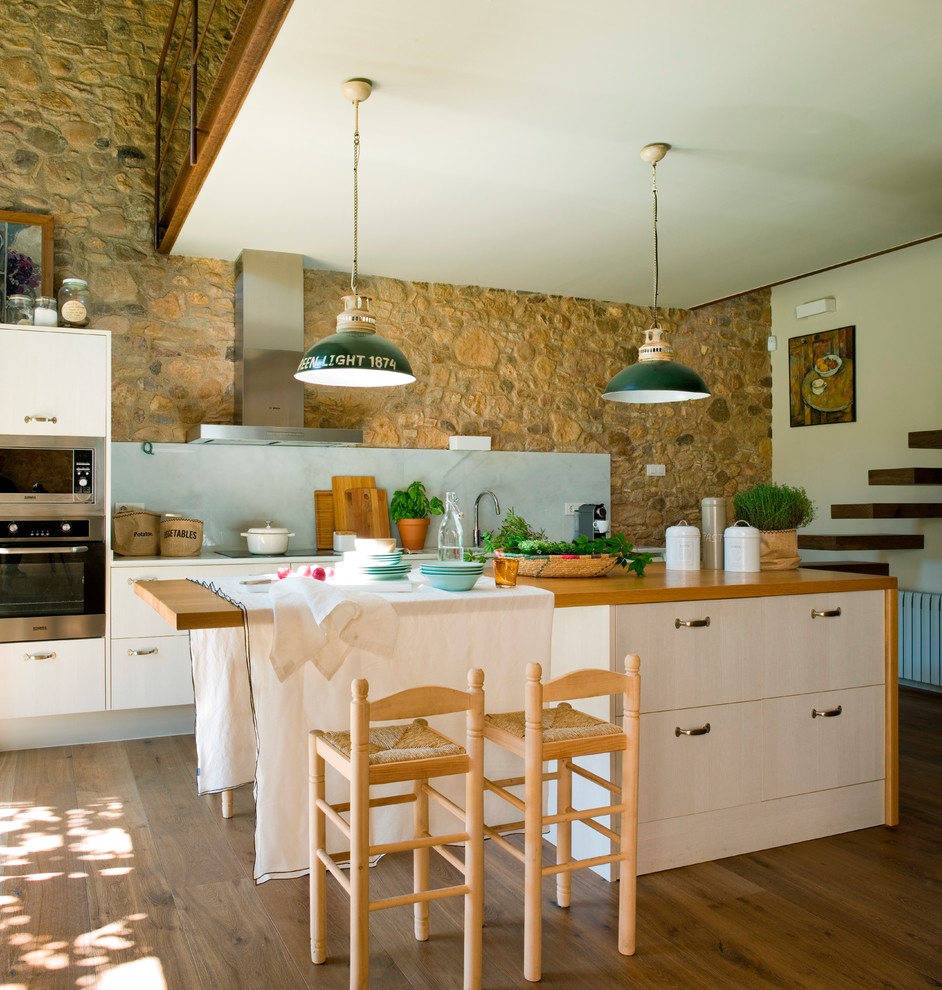 Photo of a mid-sized country galley kitchen in Barcelona with flat-panel cabinets, beige cabinets, wood benchtops, grey splashback, stone slab splashback, stainless steel appliances, medium hardwood floors and with island.