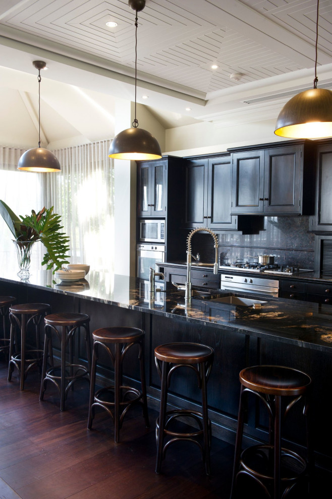 This is an example of an expansive country single-wall open plan kitchen in Central Coast with a double-bowl sink, recessed-panel cabinets, black cabinets, onyx benchtops, black splashback, granite splashback, stainless steel appliances, dark hardwood floors, with island, brown floor and black benchtop.