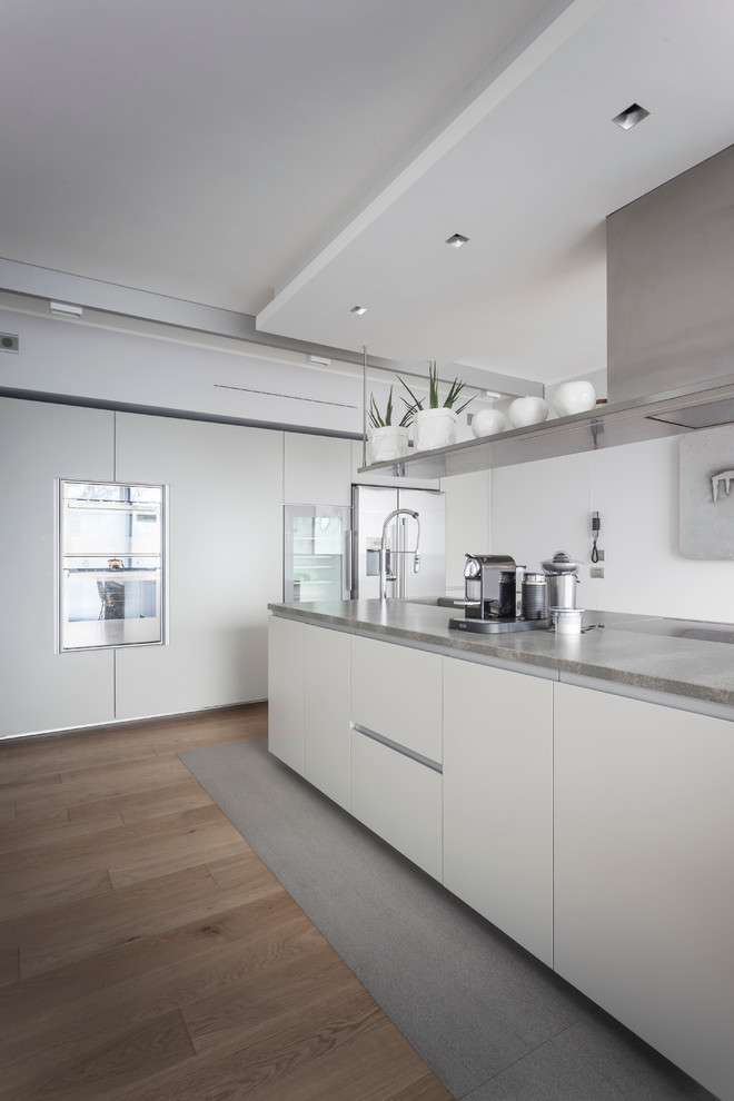 This is an example of a large contemporary kitchen in Milan with flat-panel cabinets, white cabinets, granite benchtops, stainless steel appliances, light hardwood floors and with island.