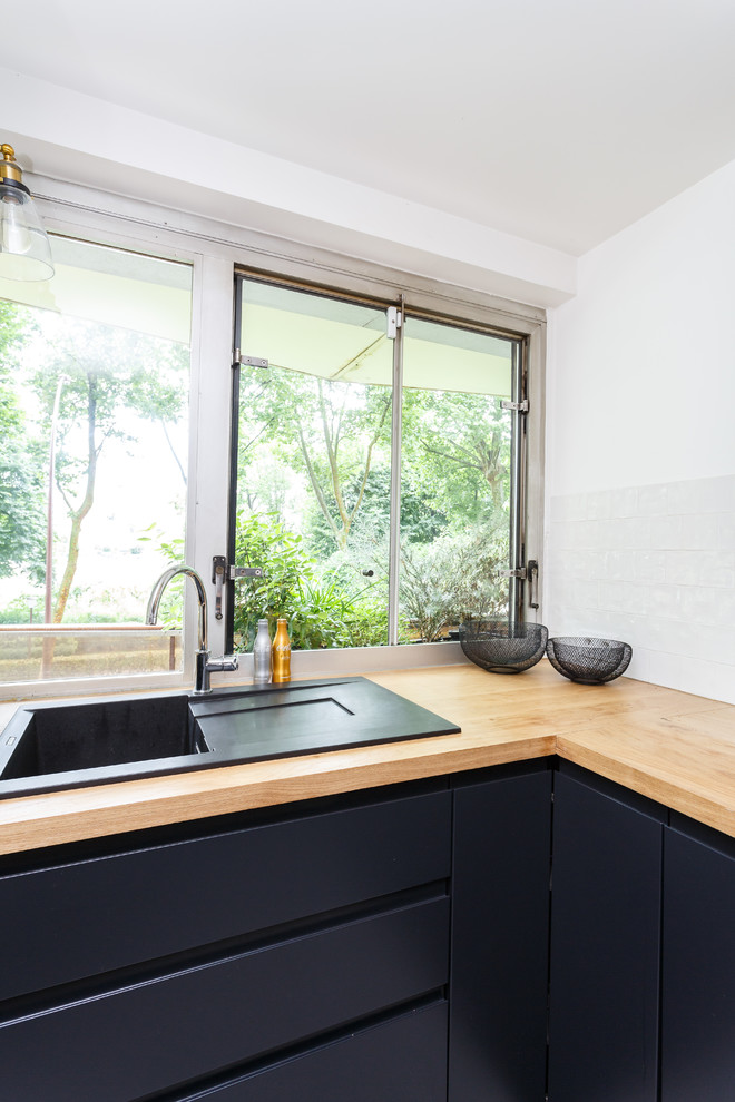 Photo of a small scandinavian l-shaped separate kitchen in Paris with a drop-in sink, flat-panel cabinets, black cabinets, wood benchtops, white splashback, ceramic splashback, stainless steel appliances, terrazzo floors, no island, multi-coloured floor and brown benchtop.