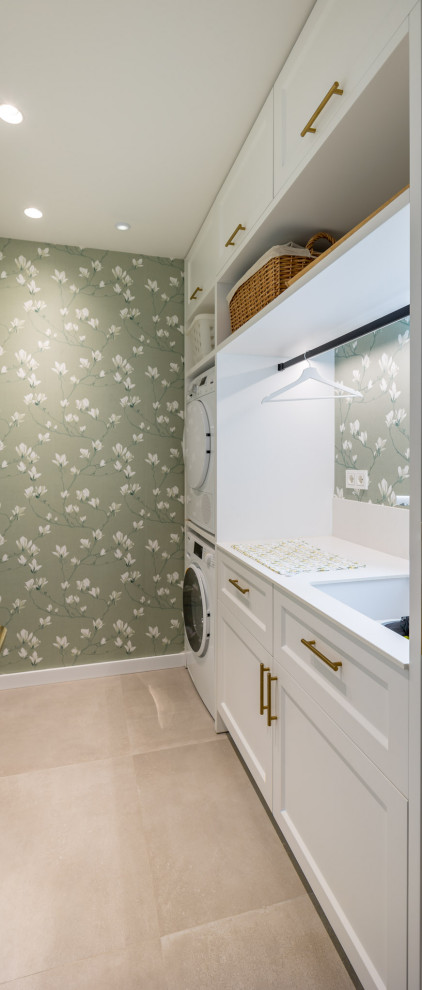 Inspiration for a mid-sized mediterranean single-wall dedicated laundry room in Alicante-Costa Blanca with an undermount sink, raised-panel cabinets, white cabinets, quartz benchtops, green walls, porcelain floors, a stacked washer and dryer, grey floor, white benchtop and wallpaper.