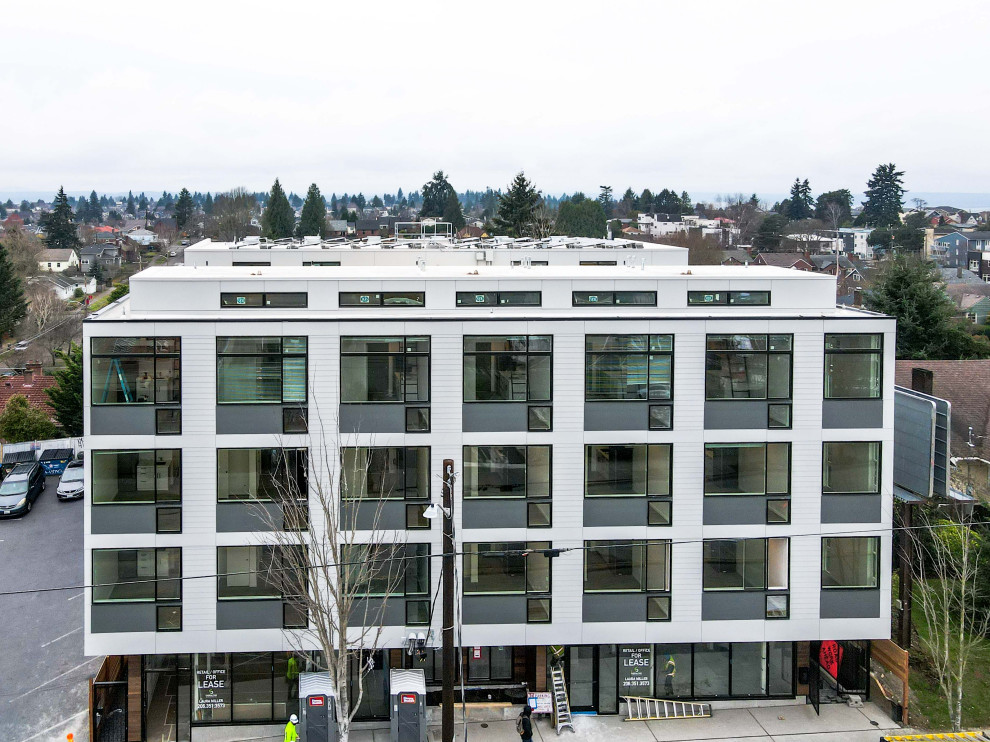 Expansive and white modern flat in Seattle with four floors, concrete fibreboard cladding, a flat roof, a mixed material roof, a white roof and board and batten cladding.