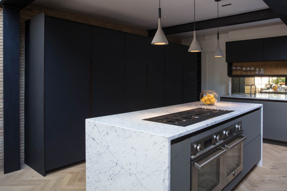 Photo of a large contemporary l-shaped open plan kitchen in London with a farmhouse sink, flat-panel cabinets, grey cabinets, laminate benchtops, brown splashback, brick splashback, panelled appliances, light hardwood floors, with island, beige floor and white benchtop.