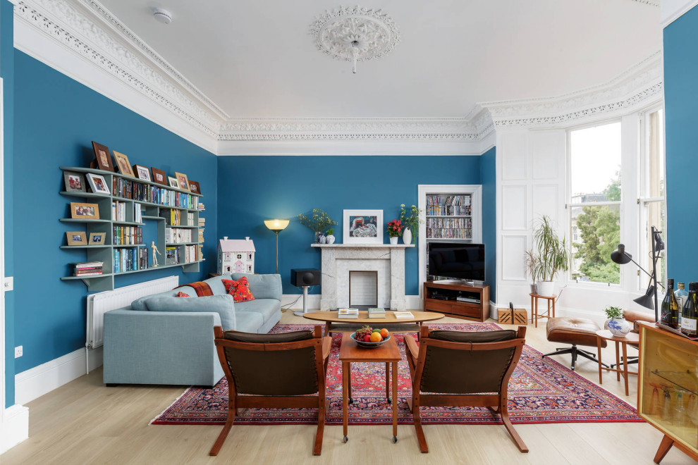 Photo of a transitional open concept living room in Edinburgh with blue walls, a standard fireplace, a stone fireplace surround, light hardwood floors, a freestanding tv and beige floor.