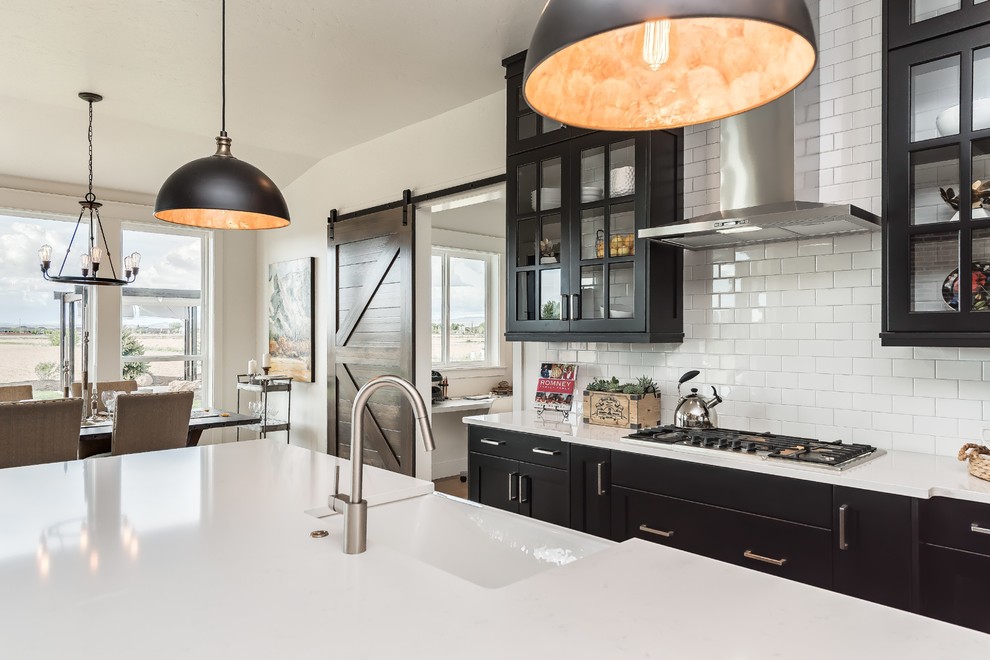 Design ideas for an expansive country eat-in kitchen in Boise with a farmhouse sink, glass-front cabinets, black cabinets, quartz benchtops, white splashback, stainless steel appliances, with island and subway tile splashback.