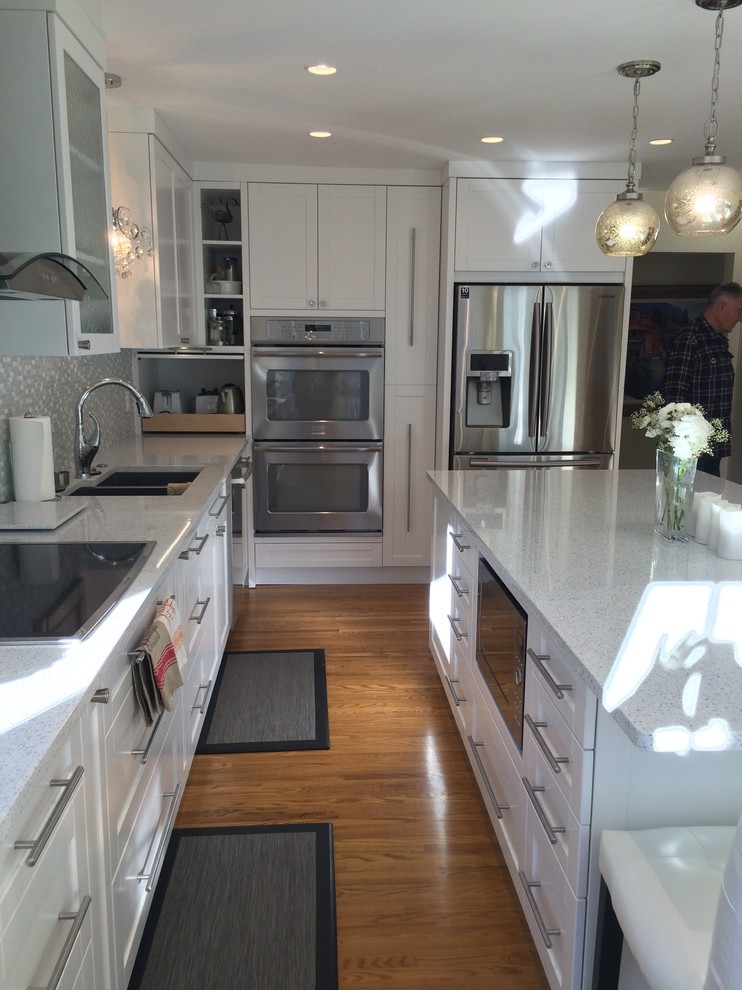 Photo of a mid-sized transitional l-shaped separate kitchen in Calgary with an undermount sink, shaker cabinets, white cabinets, solid surface benchtops, white splashback, mosaic tile splashback, stainless steel appliances, medium hardwood floors and with island.