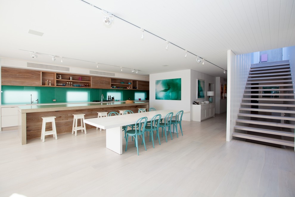 Design ideas for a large beach style galley eat-in kitchen in Sydney with a double-bowl sink, flat-panel cabinets, medium wood cabinets, concrete benchtops, blue splashback, glass sheet splashback, panelled appliances, light hardwood floors and with island.