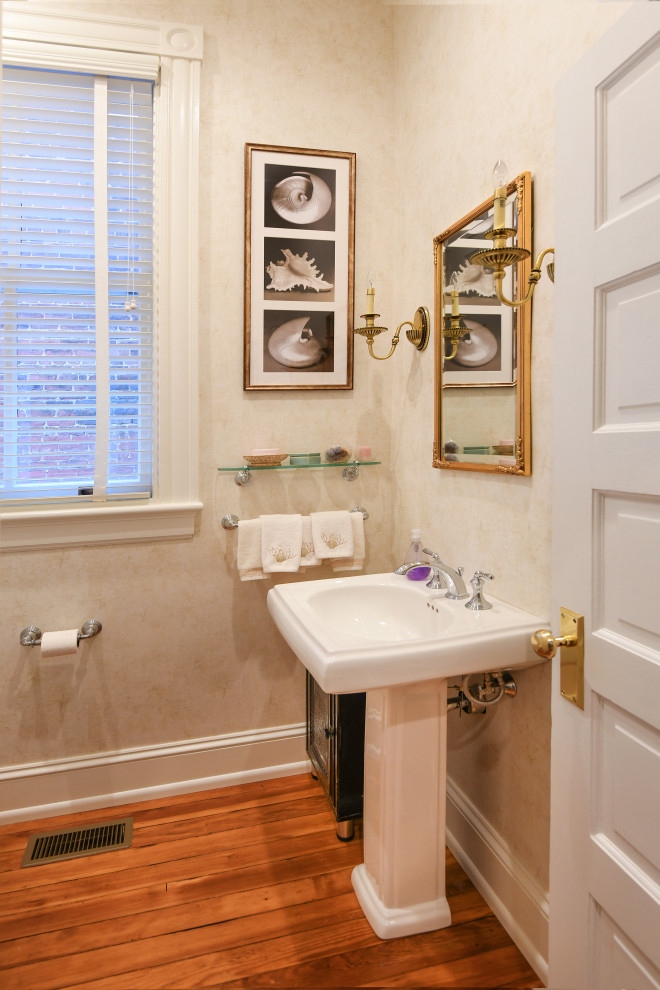 Photo of a small traditional powder room in Richmond with beige walls, medium hardwood floors, a pedestal sink, brown floor and wallpaper.
