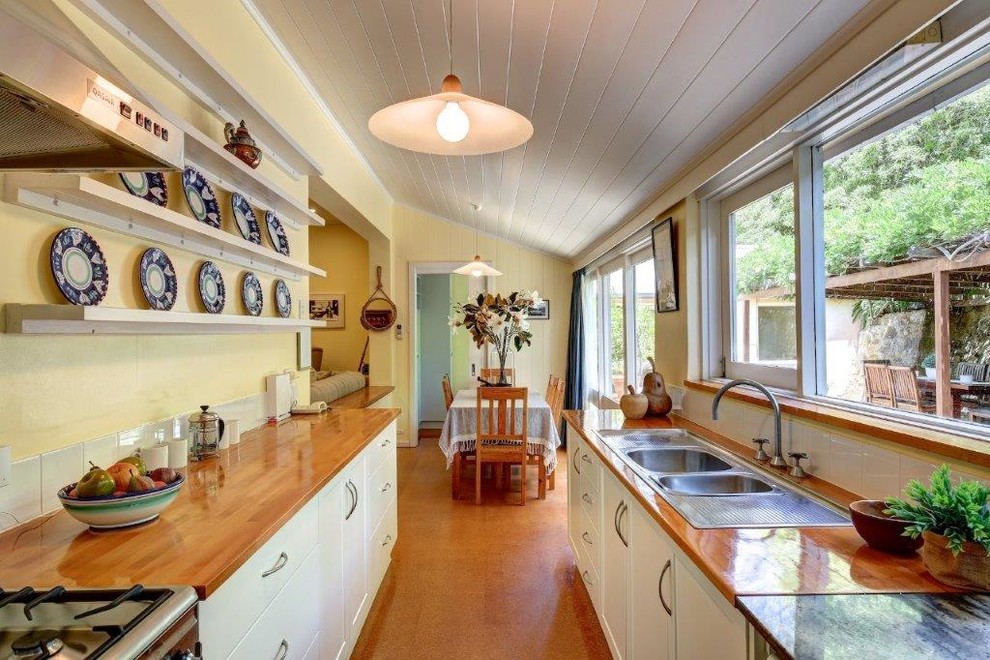 Photo of a mid-sized country galley eat-in kitchen in Adelaide with a double-bowl sink, recessed-panel cabinets, white cabinets, wood benchtops, white splashback, ceramic splashback, stainless steel appliances, cork floors, beige floor and beige benchtop.