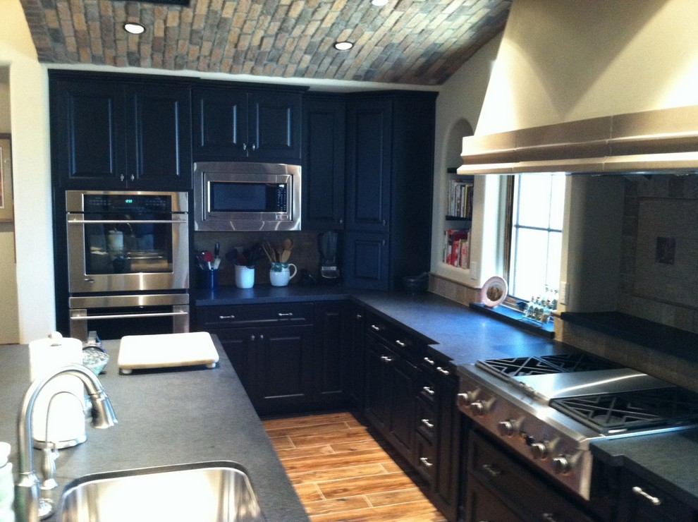Eat-in kitchen - mid-sized transitional l-shaped light wood floor and brown floor eat-in kitchen idea in Phoenix with a double-bowl sink, raised-panel cabinets, granite countertops, white backsplash, stainless steel appliances, black cabinets, ceramic backsplash and an island