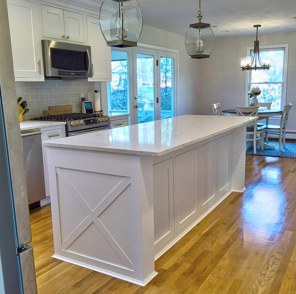 Inspiration for a mid-sized transitional l-shaped eat-in kitchen in Boston with a farmhouse sink, shaker cabinets, white cabinets, quartzite benchtops, beige splashback, subway tile splashback, stainless steel appliances, light hardwood floors, with island and white benchtop.