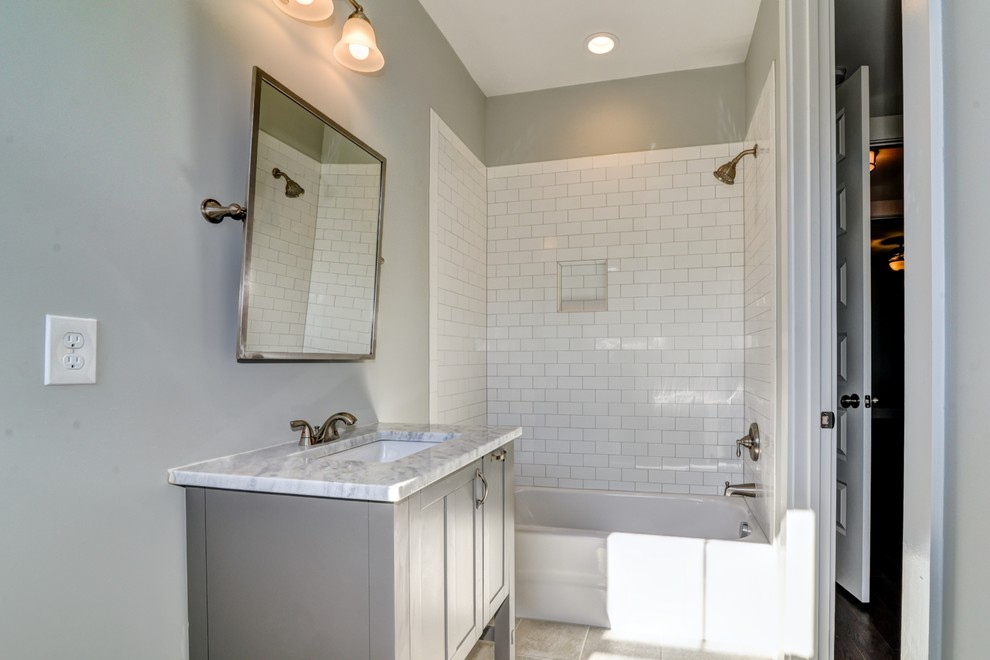 Design ideas for a large transitional bathroom in Charlotte with shaker cabinets, grey cabinets, an alcove tub, a shower/bathtub combo, white tile, subway tile, grey walls, ceramic floors, an undermount sink, marble benchtops and brown floor.