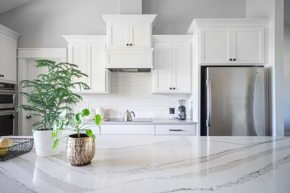 Photo of a large transitional l-shaped open plan kitchen in Portland with an undermount sink, shaker cabinets, white cabinets, marble benchtops, white splashback, subway tile splashback, stainless steel appliances, medium hardwood floors, with island, beige floor and white benchtop.