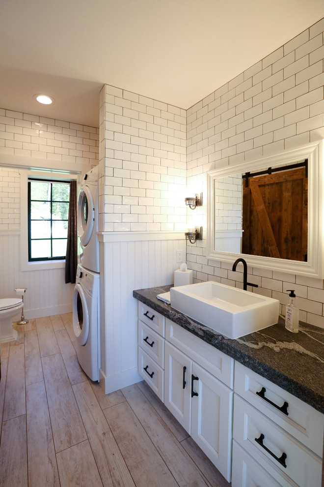 This is an example of a mid-sized transitional master bathroom in Other with recessed-panel cabinets, white cabinets, an open shower, a two-piece toilet, white tile, subway tile, white walls, light hardwood floors, a vessel sink, soapstone benchtops and a laundry.