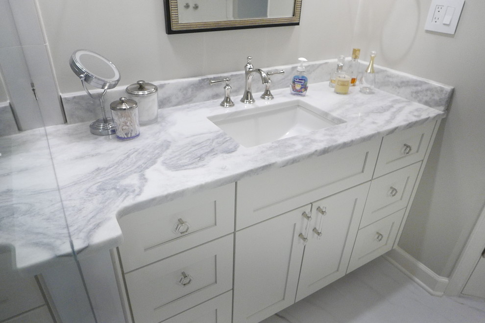 Inspiration for a large transitional master white tile and porcelain tile porcelain tile and white floor freestanding bathtub remodel with shaker cabinets, white cabinets, a two-piece toilet, beige walls, an undermount sink, marble countertops, a hinged shower door and white countertops