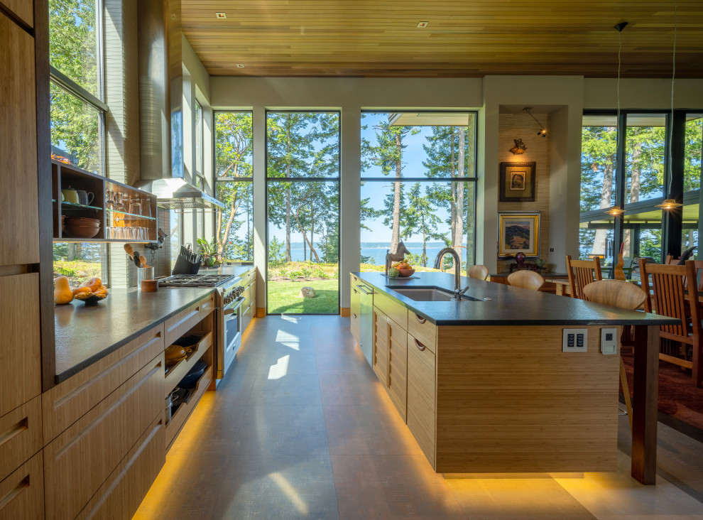This is an example of a mid-sized modern l-shaped open plan kitchen in Seattle with an undermount sink, flat-panel cabinets, light wood cabinets, granite benchtops, green splashback, glass tile splashback, stainless steel appliances, porcelain floors, with island, grey floor, black benchtop and wood.
