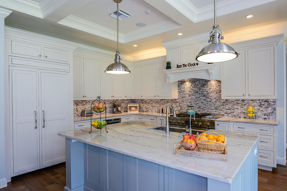 Photo of a large transitional l-shaped open plan kitchen in Tampa with a farmhouse sink, beaded inset cabinets, white cabinets, quartzite benchtops, metallic splashback, glass tile splashback, stainless steel appliances, light hardwood floors and with island.