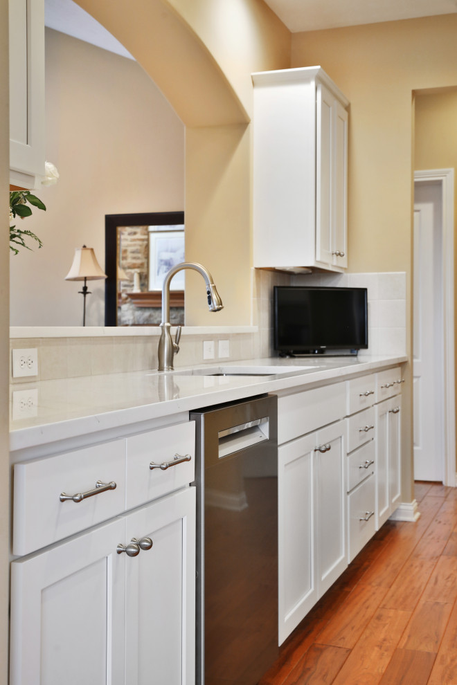 Example of a mid-sized transitional galley medium tone wood floor and brown floor enclosed kitchen design in Columbus with a single-bowl sink, shaker cabinets, white cabinets, quartz countertops, white backsplash, ceramic backsplash, stainless steel appliances, no island and white countertops